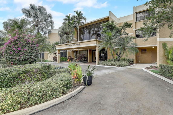Front view of a multi-story building with a driveway and greenery.
