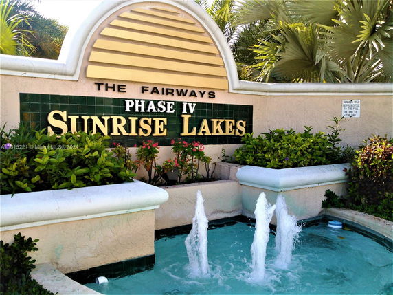 Entrance sign for Sunrise Lakes Phase IV with a water fountain and greenery.