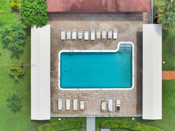 Aerial view of a rectangular swimming pool surrounded by lounge chairs and shaded areas.