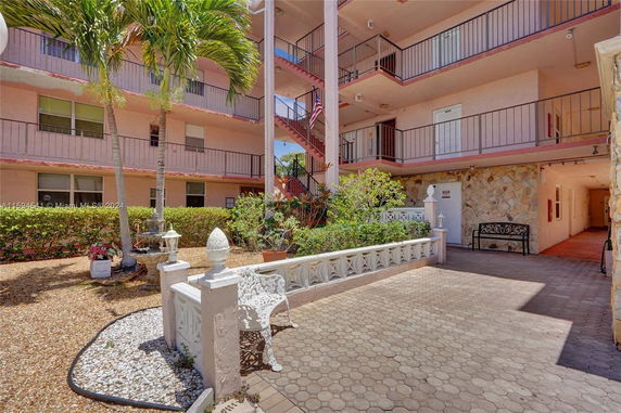 Front view of a multi-story apartment building with open corridors and decorative landscaping.