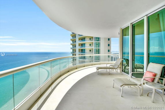 Panoramic ocean view from a high-rise balcony with glass railing and outdoor seating.