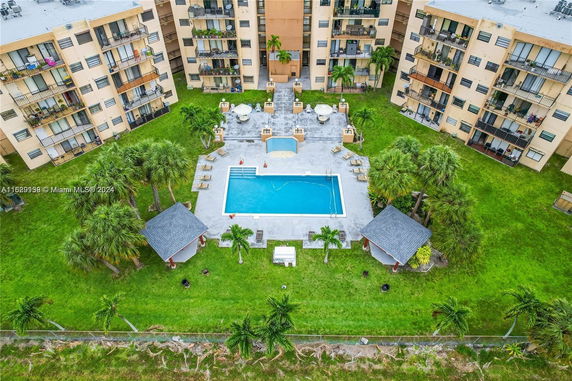 Aerial view of an apartment complex featuring a central swimming pool area surrounded by green lawns and palm trees.