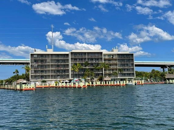 View of a multi-story waterfront building with balconies and a nearby bridge.