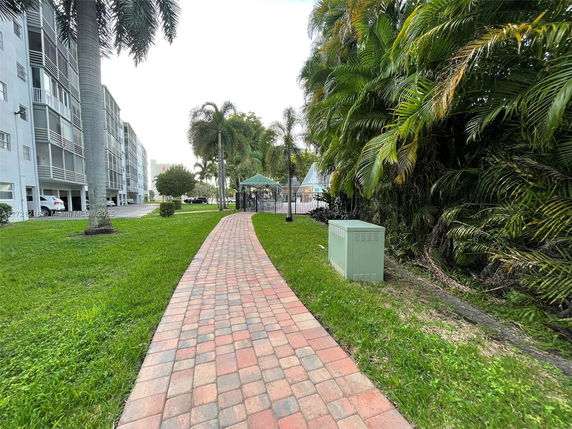Pathway beside a multi-story residential building with palm trees and greenery.