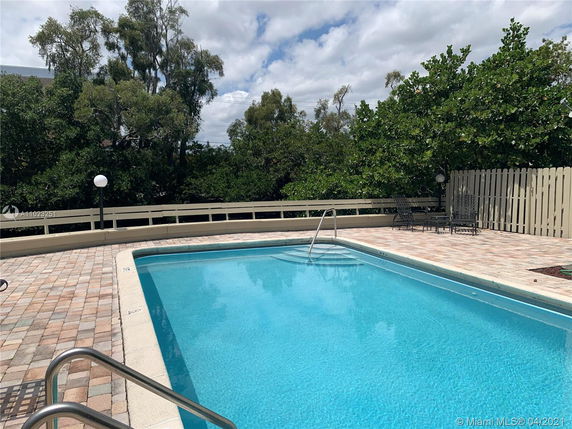 Image of an outdoor swimming pool with surrounding patio area and greenery.