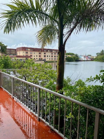 View of residential buildings across a body of water with trees and a wet pathway in the foreground.