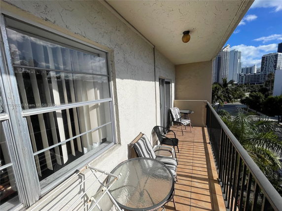 Balcony view overlooking city buildings with outdoor chairs and a table.