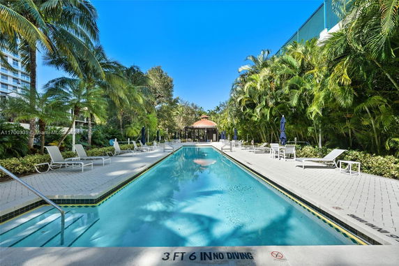 Outdoor swimming pool with lounge chairs and surrounding tropical vegetation.