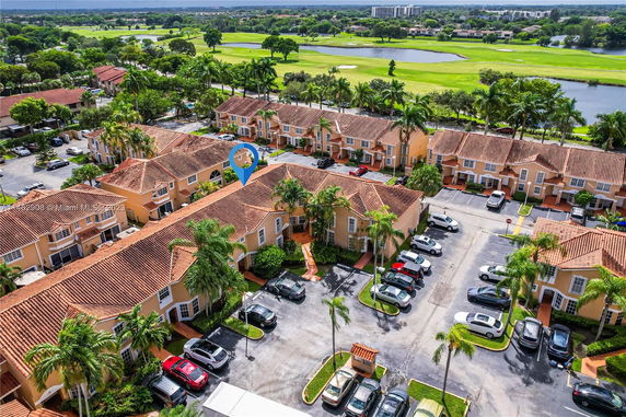 Aerial view of a residential complex with multiple two-story houses featuring red-tiled roofs and spacious parking areas, surrounded by greenery and golf course.