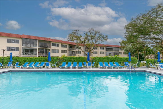 Outdoor swimming pool area in front of a residential building with red-tiled roofs.
