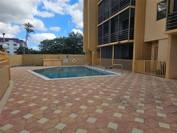 Outdoor swimming pool area beside a multi-story building with railing.