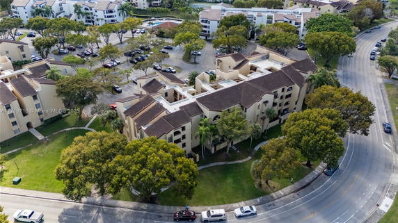 Aerial view of a residential complex with multiple beige buildings and parking areas surrounded by trees.