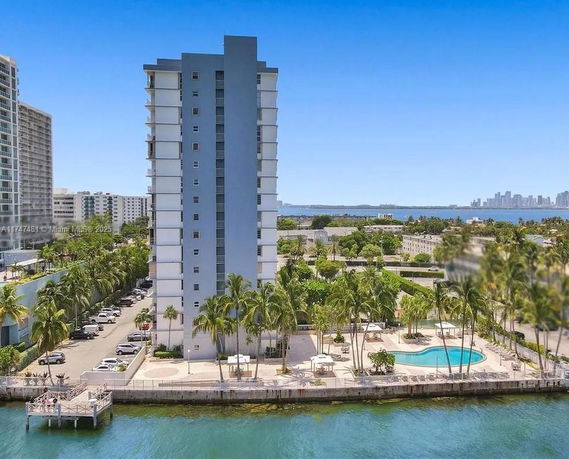Front view of a tall residential building by the water with a swimming pool area.