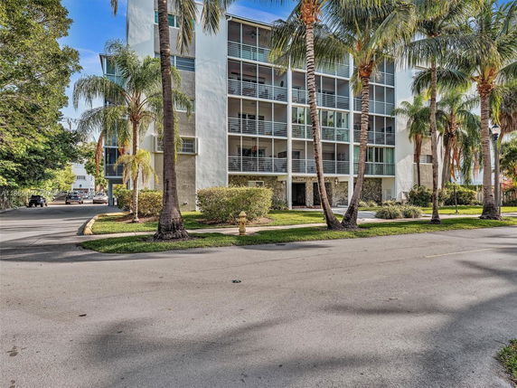 Front view of a multi-story building with balconies and palm trees in front.