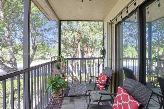 Screened balcony with outdoor seating and plants, overlooking trees and street.