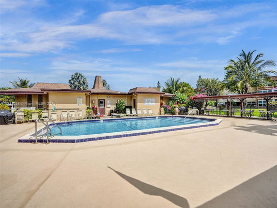 Outdoor swimming pool area with surrounding seating and a small building.