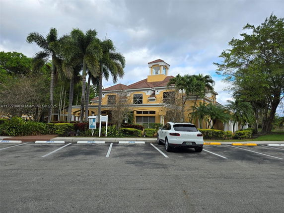 Front view of a large two-story building with prominent palm trees and a parking area.
