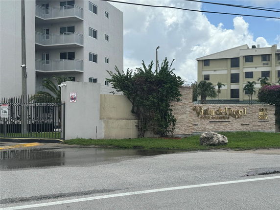 Front view of a multi-story condominium building with balconies and a gated entrance.