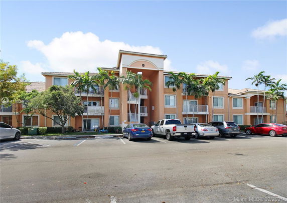 Front view of a multi-story apartment building with balconies and a parking area in front.