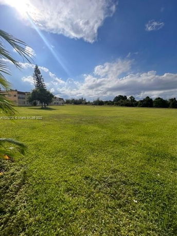 Expansive grassy field on a sunny day with buildings in the distance.
