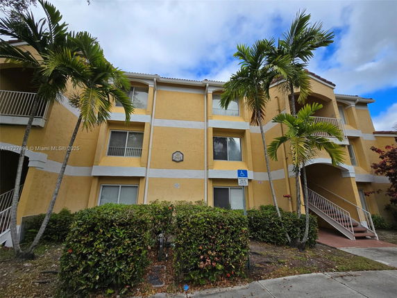 Front view of a three-story residential building with balconies and staircase entrances.