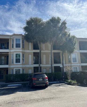 Front view of a three-story residential building with palm trees in front.