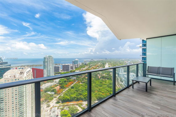 View from a high-rise balcony overlooking a cityscape with tall buildings and a coastline in the distance.