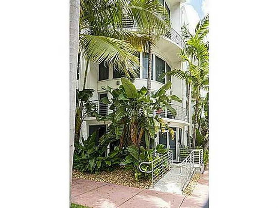 Front view of a multi-story building with balconies and surrounding palm trees.