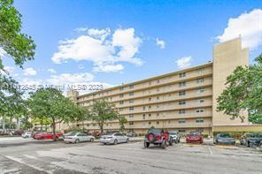Front view of a multi-story apartment building with multiple balconies and a parking lot.