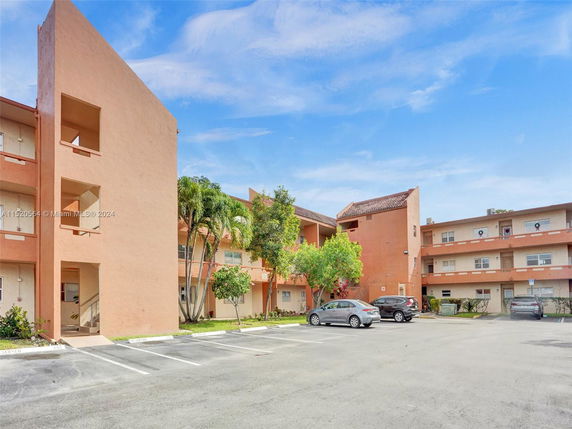 Front view of a multi-story apartment building with balconies and parking area.