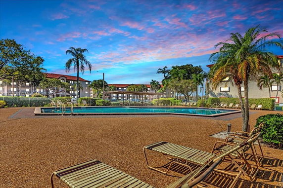 Outdoor swimming pool area with lounge chairs and nearby buildings.