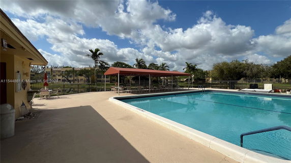 Outdoor swimming pool area with lounge chairs and a shaded canopy.
