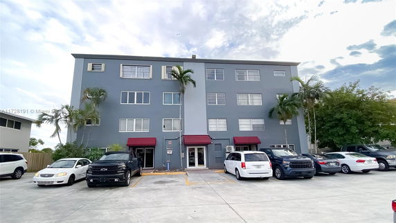 Front view of a multi-story apartment building with multiple windows and a parking area in front.