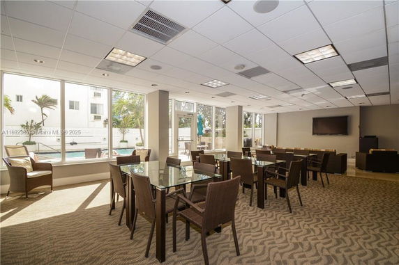 Common area with tables and chairs, large windows, and a television.
