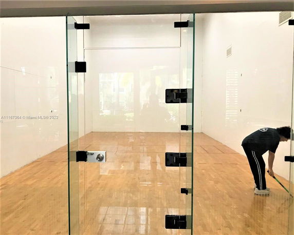 Indoor squash or racquetball court with wooden flooring and glass door.