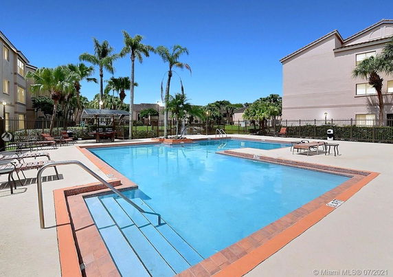 Outdoor swimming pool area with surrounding buildings and palm trees.