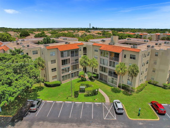 Front view of a multi-story apartment complex with red-tiled roofs and parking area in front.