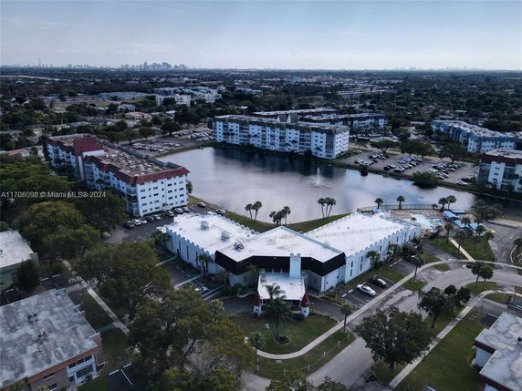 Aerial view of residential buildings surrounding a small lake with parking areas and a swimming pool.