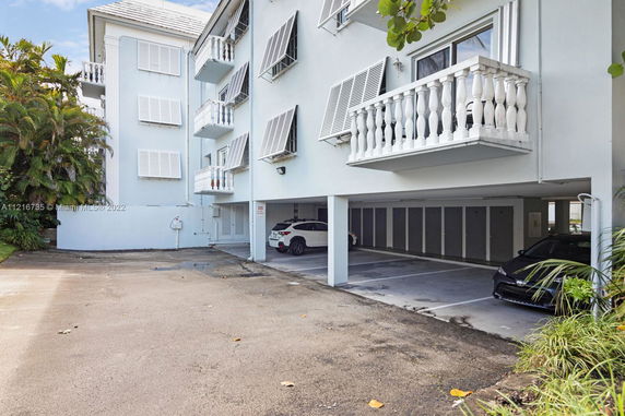 Outdoor parking area beneath a multi-story building with angled shutters and balconies.