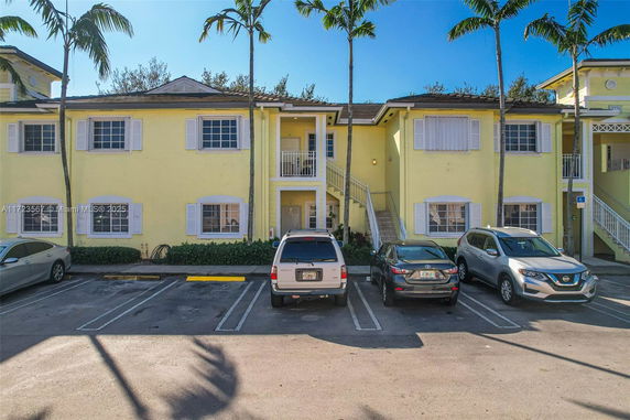Parking area in front of a two-story yellow apartment building with palm trees.