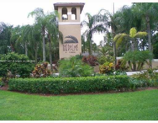 Front view of a building entrance sign with palm trees and landscaping.