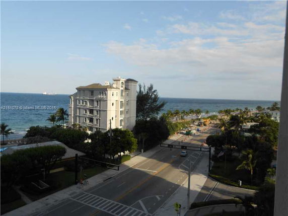 View of a multi-story building near the coast, with roads and palm trees in the surrounding area.