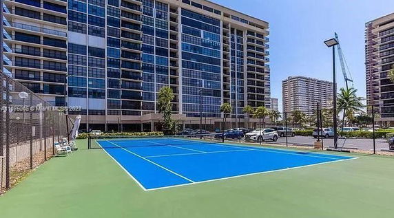 Front view of a high-rise apartment building with glass facades, adjacent to a tennis court.