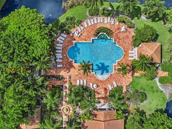 Aerial view of an outdoor swimming pool with surrounding patio and greenery.