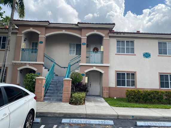 Front view of a two-story apartment building with external stairs and reserved parking spaces.