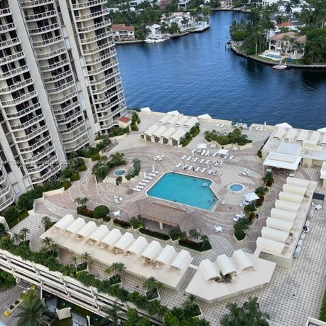 Aerial view of a pool area with lounge chairs and surrounding high-rise buildings overlooking a body of water.