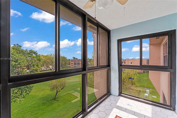 View from a sunlit balcony with glass windows overlooking a grassy area and nearby buildings.