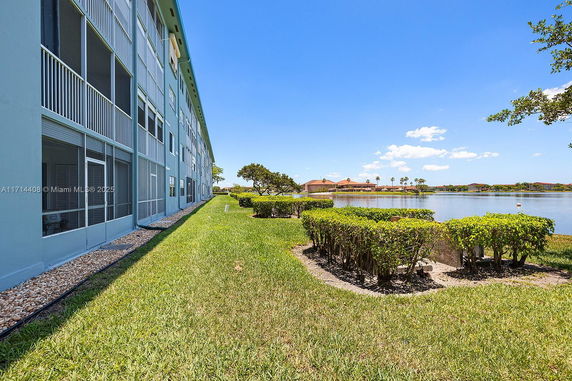 Side view of a multi-story building next to a lake with landscaped greenery.