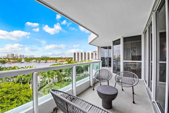 Balcony view from a modern apartment overlooking a cityscape with tall buildings and greenery.