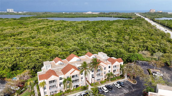 Building surrounded by lush greenery and distant water bodies with a parking area in the foreground.